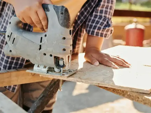 Ręce trzymają wyrzynarkę, która tnie deskę OSB.