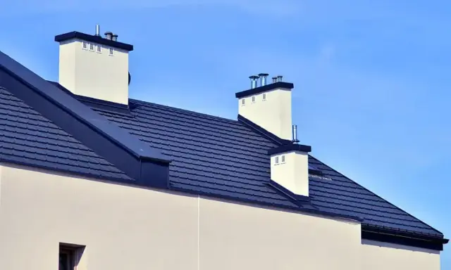 Nowoczesny dach bez okapu konstrukcja z ciemnogranatową dachówką i białymi kominami.