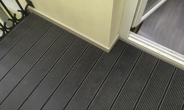 Ciemnoszara deska kompozytowa pełna, tworząca nowoczesną podłogę tarasu, z widocznym fragmentem drzwi balkonowych i jasną ścianą.