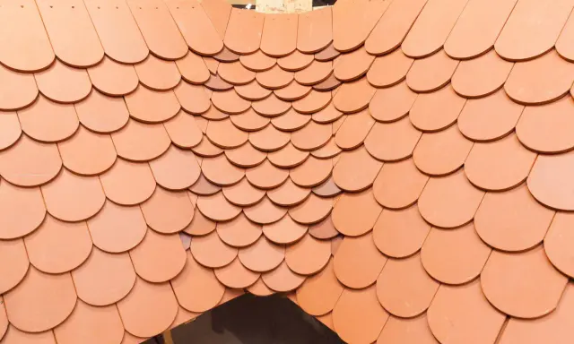 Obróbka kosza lukarny z dachówki ceramicznej. Widok z góry na ułożone dachówki, tworzące łukowaty kształt.