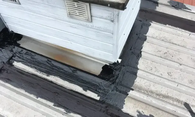 Uszczelnianie dachu, gdzie dach przecieka na wkrętach. Czarna masa izolacyjna na białej blasze.