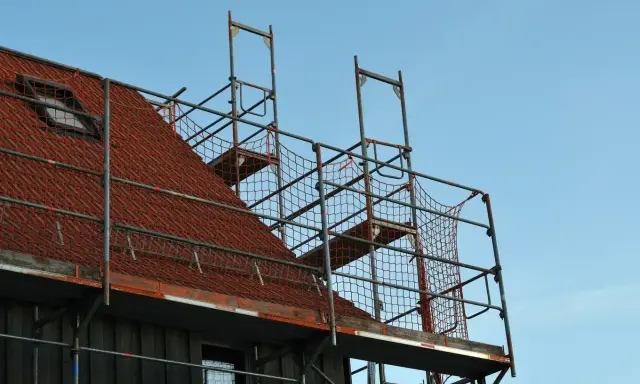 Metalowe rusztowanie na dachu z czerwonej dachówki, gotowe do prac remontowych.