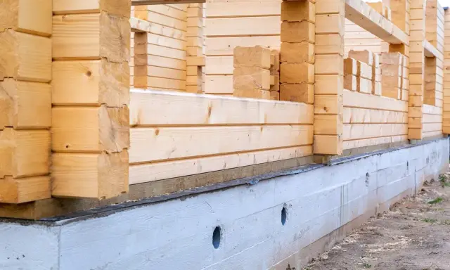 Drewniana konstrukcja domu opiera się na solidnym betonowym fundamencie. Pokazuje to, jak połączyć drewno z betonem w budownictwie.