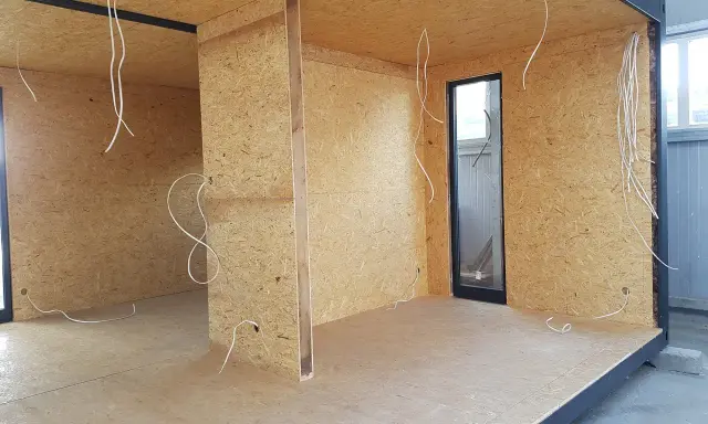Budowa ścianki działowej z drewna: widok wnętrza z płyt OSB, instalacją elektryczną i oknem.