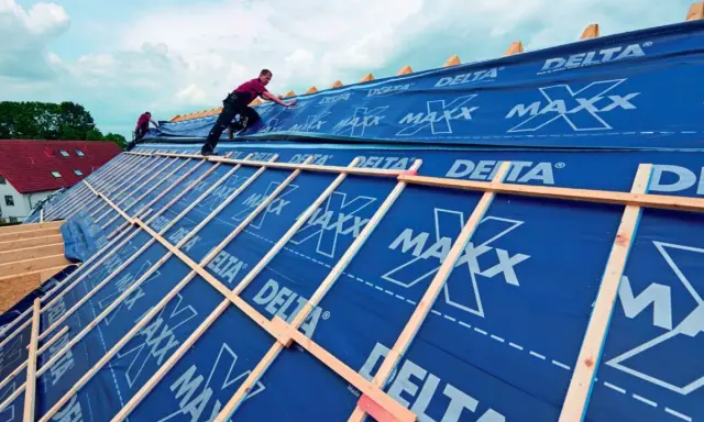 Dach krążynowy w budowie, pracownicy układają niebieską membranę DELTA MAXX na drewnianej konstrukcji.