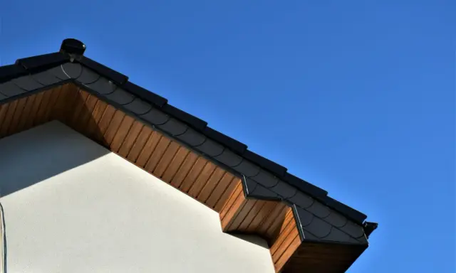 Elegancka podbitka z płyty OSB pod ciemnym dachem, kontrastująca z jasną elewacją i błękitem nieba.