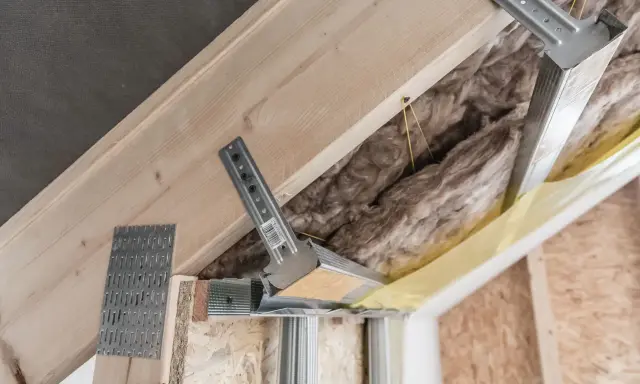 Konstrukcja poddasza z wełną mineralną i profilem metalowym. Widać elementy montażowe, które mogą być używane jako wkręty do wieszaków grzybkowych.