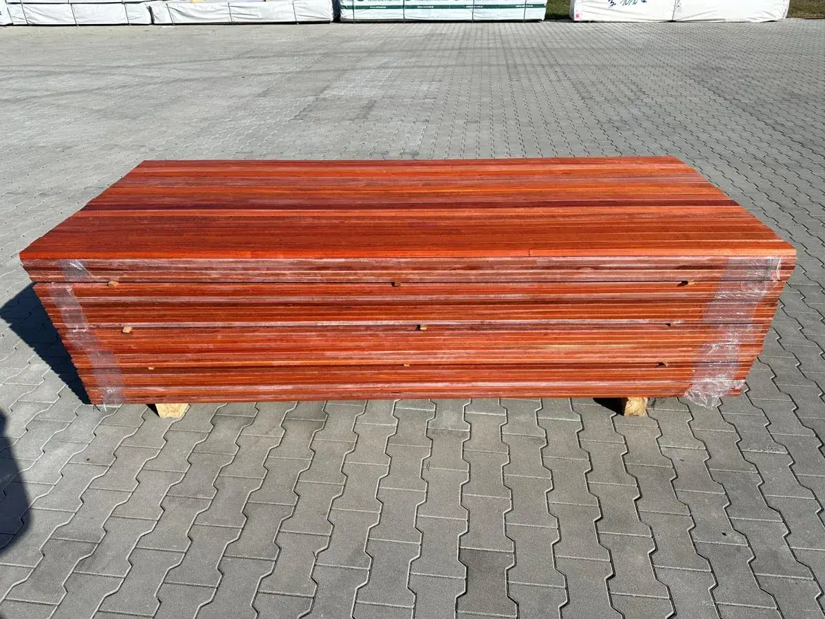Stos desek z egzotycznego padouk drewna, owinięty folią, czeka na wykorzystanie w projekcie tarasu.