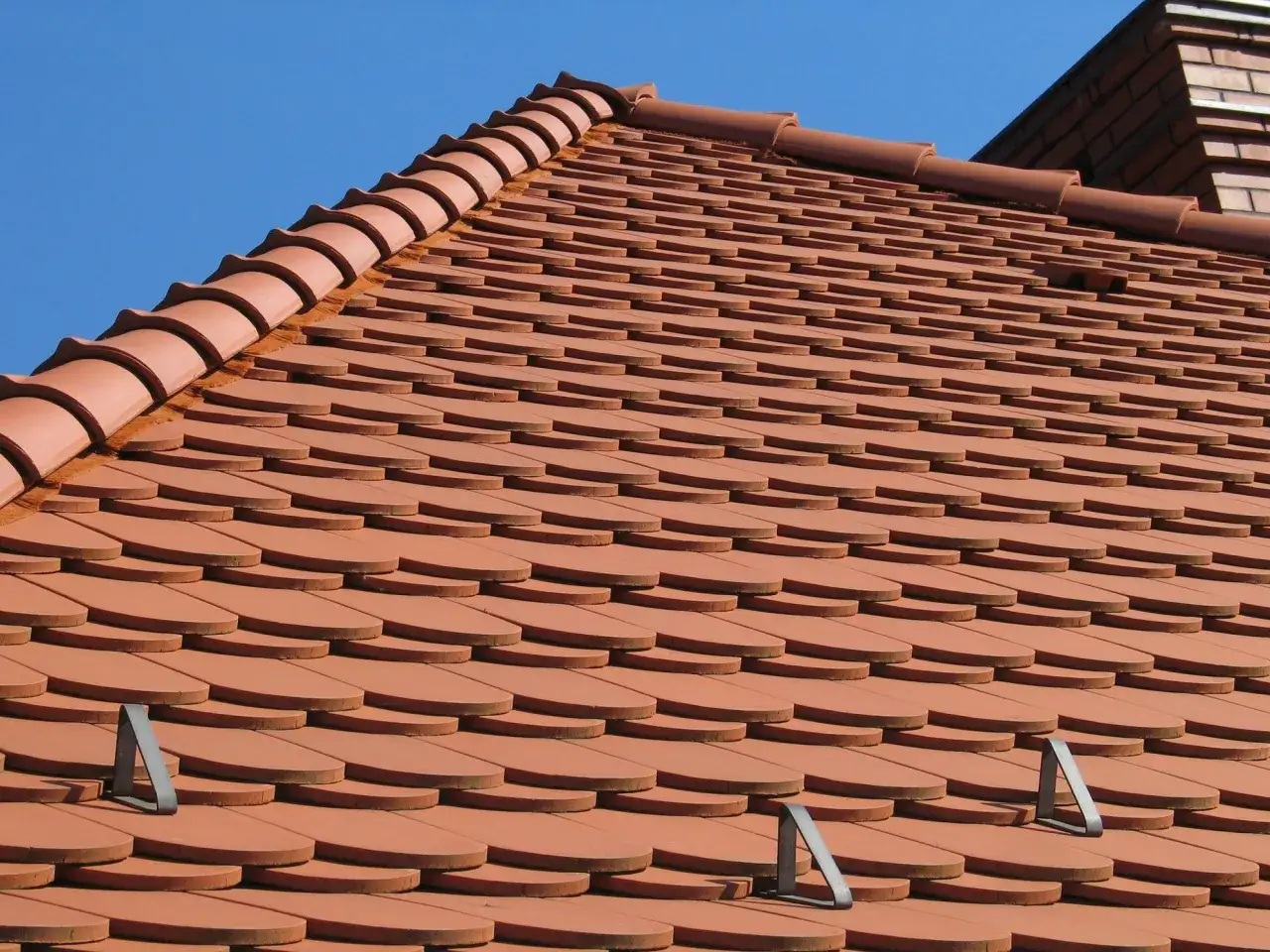 Nowy dach z dachówki ceramicznej, ułożonej w charakterystyczny wzór łuski, lśni w słońcu.